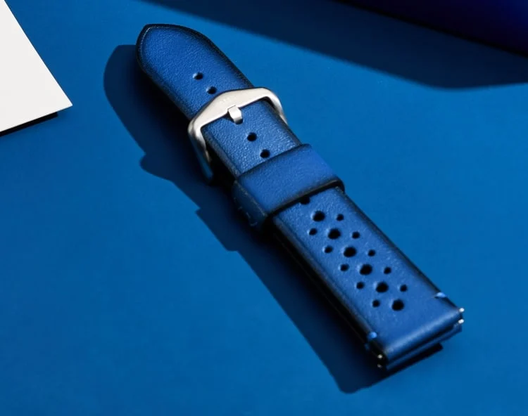 The royal blue leather strap with a perforated pattern, shown on a monochromatic deep blue background.