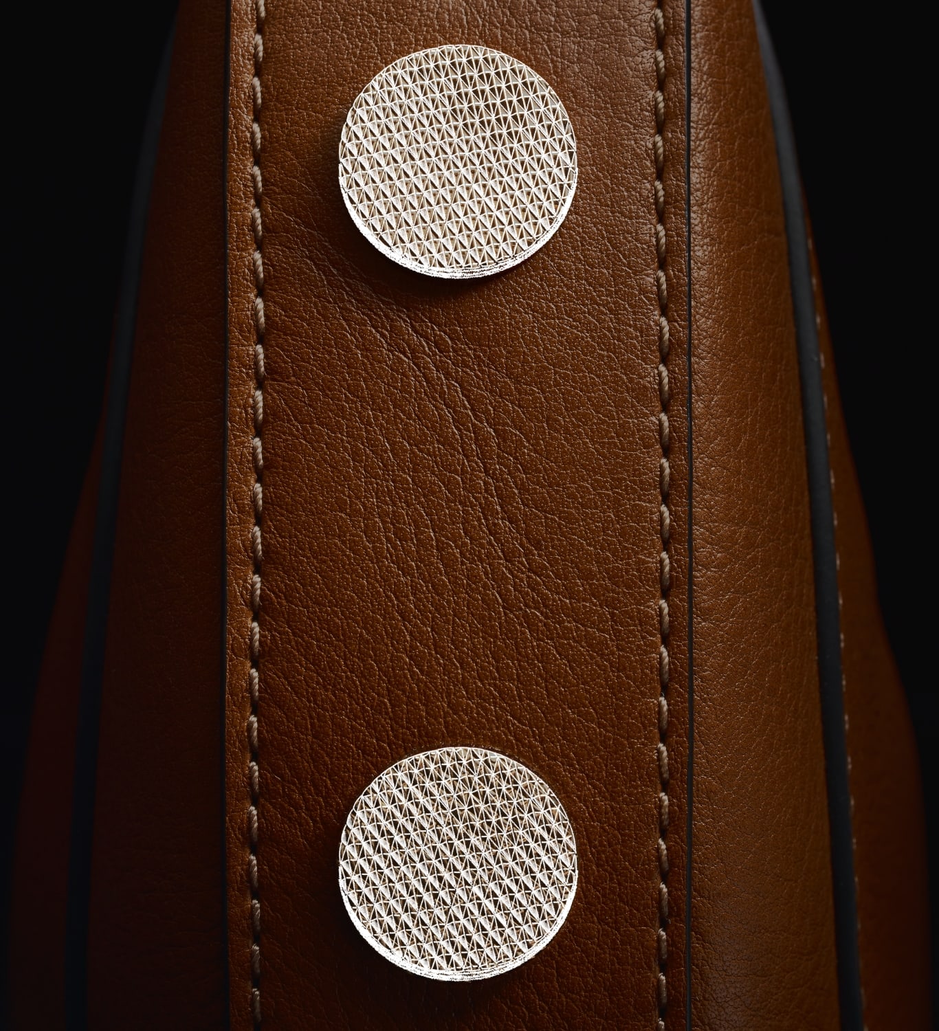 Two gold-tone knurled studs on a brown leather Harwell bag, overlaid with a sketch.