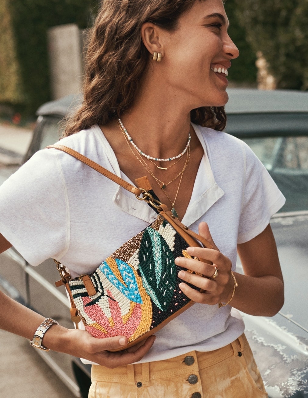 Une femme sourit, elle porte un sac Jolie en perles de la collection Beaded Resort.