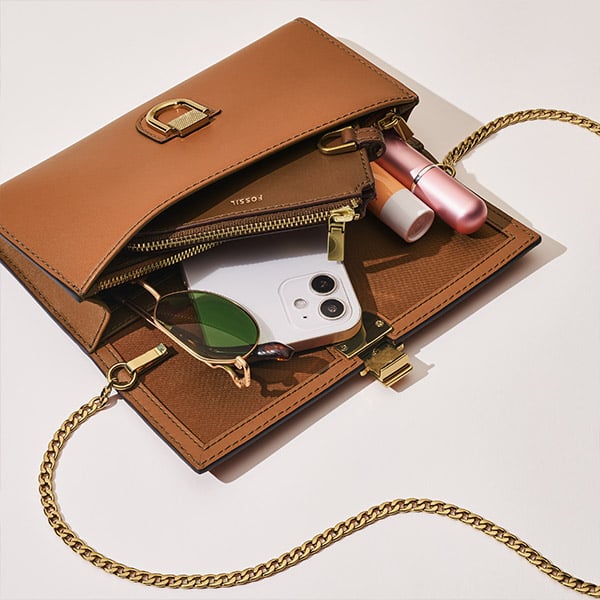 A woman lying on a brown sofa wearing the white FB-01 watch and carrying a yellow Jolie baguette.