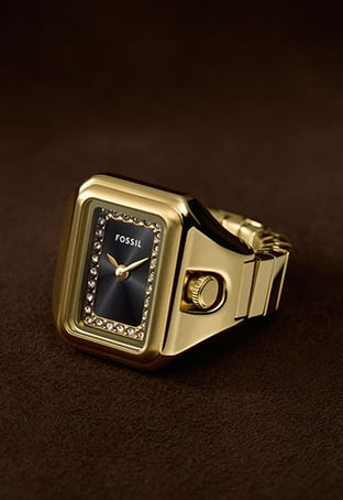 A gold-toned Raquel watch ring with a black dial and crystal embellishments sits on the pointer finger of a stylish woman as she poses.