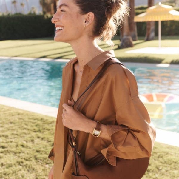 A woman smiling and wearing the brown leather Harwell bag.