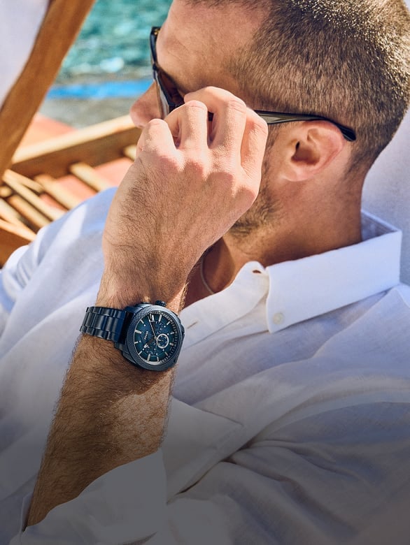 A man looking out on the water wearing sunglasses and the ocean blue Fossil Machine Chronograph watch.