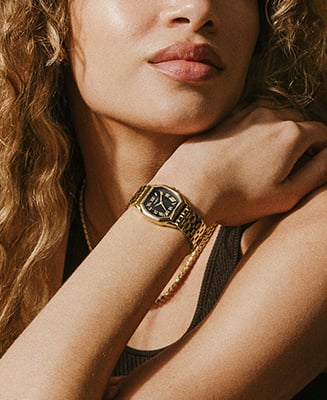 Ein Lifestyle-Bild einer Frau, die eine goldfarbene Uhr Harlow mit schwarzem Zifferblatt trägt.