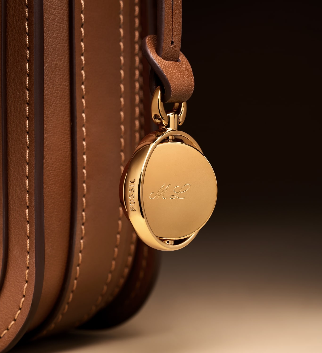 The gold-tone Legacy Charm hanging from the brown leather Lennox bag and engraved with ML. Overlaid with a sketch.