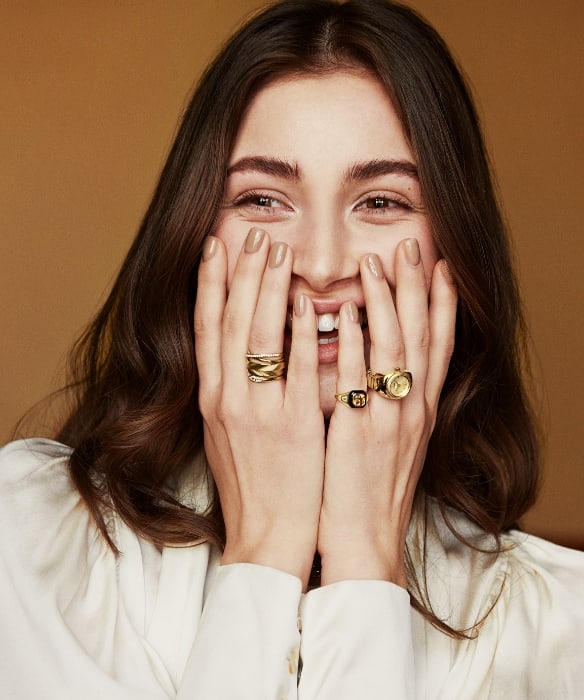 A woman smiling and wearing various gold-tone rings. 