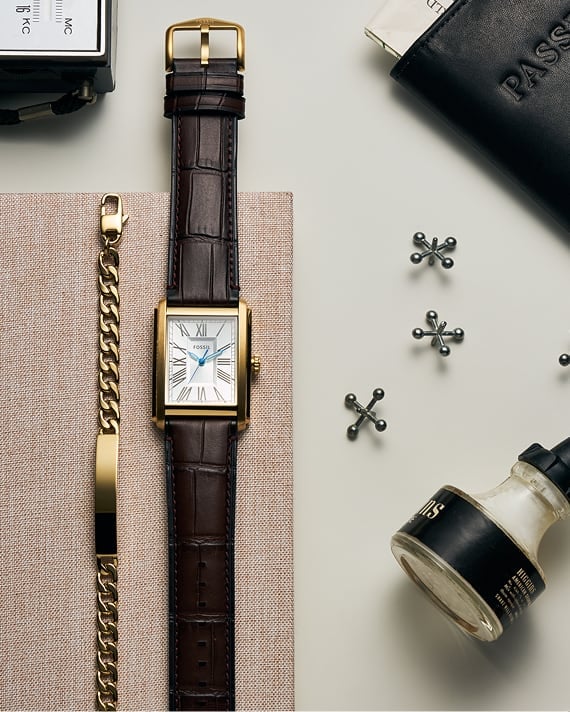 Draufsicht auf einen Schreibtisch mit einem Fossil Band ID für Herren und einer goldfarbenen Fossil Uhr Carraway mit braunem Lederband in Kroko-Optik