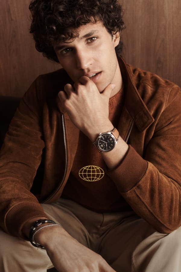 World graphic. A man wearing a Fossil Heritage watch with brown leather strap.