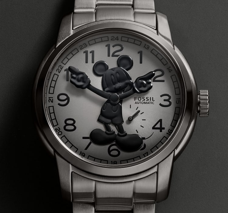 A silver-tone watch with a gradient dark gray dial featuring Disney's Mickey Mouse. His silhouette is made to look like his shadow, in glossy three-dimensional black. Mickey's gloved hands rotate to tell the time. The watch is set against a coordinating off-white background.