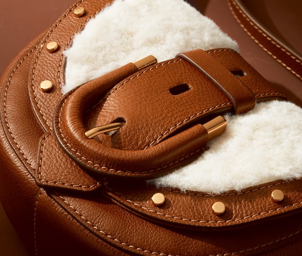 A closeup of the Harwell Mini crossbody in leather and faux shearling, featuring its leather-wrapped hardware and gold-tone studs.