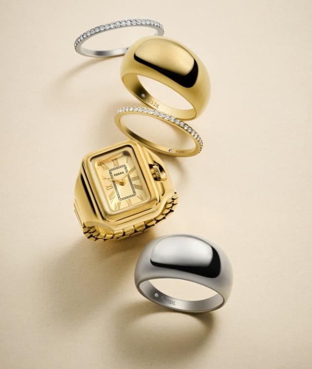 A stack of gold-tone and silver-tone rings, including a Raquel watch ring.