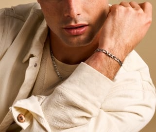 Ein Mann in cremefarbenem Hemd mit silberfarbener Halskette und silberfarbenem Armband.