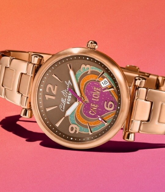 Gold-tone Cedella Marley x Fossil watch on a pink background.
