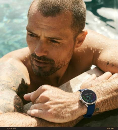 A man wearing a Gen 6 Wellness Edition smartwatch and resting on the edge of a pool.