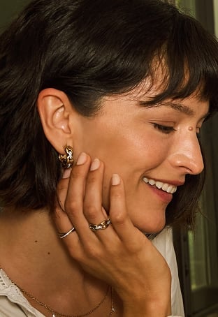 Gold-tone links and pavé crystals form sparkling hoop earrings and a ring, worn on a woman who smiles candidly.