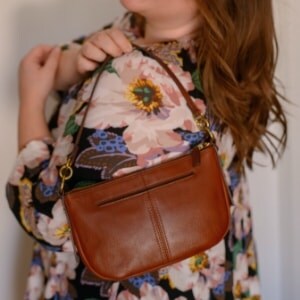 A woman in a floral dress holding a brown leather Jolie baguette.