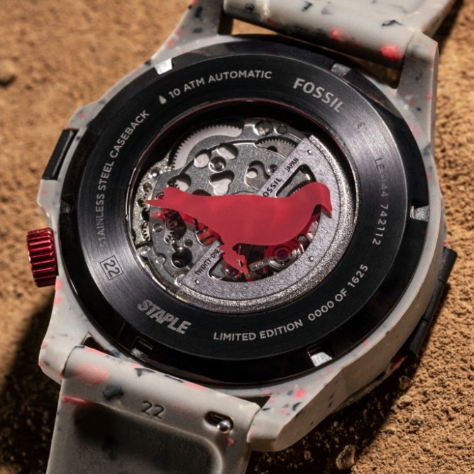 The watch's glass caseback with a pink Staple pigeon logo.