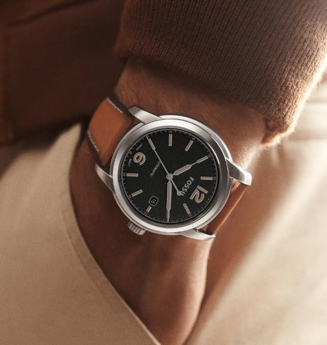 A man wearing a Fossil Heritage watch with a black dial.