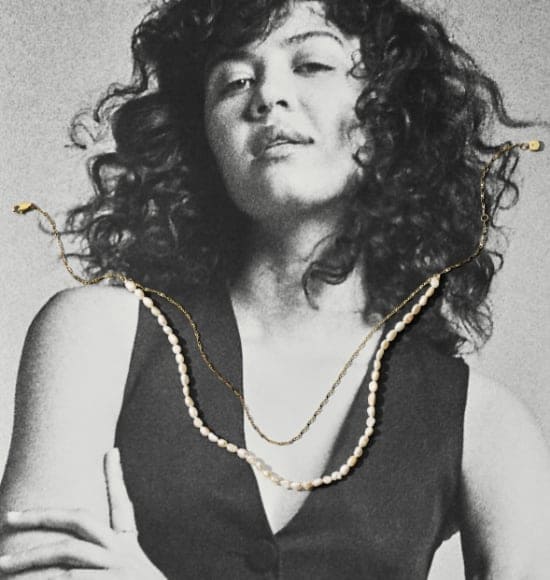 Une photo en noir et blanc d’une femme avec un collier ton or et un collier de perles d’eau douce posés sur l’image.