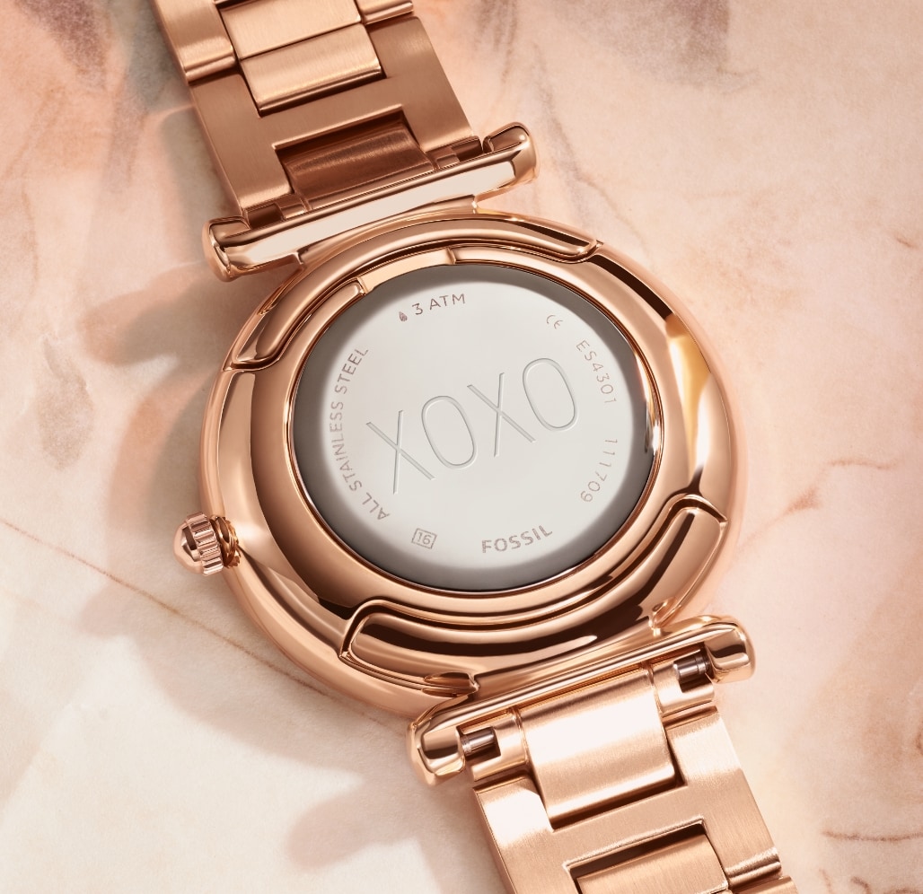 Parte trasera de un reloj en tono oro rosa con la inscripción XOXO repujada.