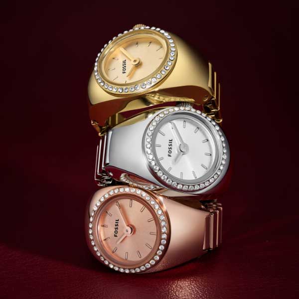 Trois bagues-montres empilées les unes sur les autres. Du bas vers le haut : ton or rose avec cristaux, ton argent avec cristaux et ton or avec cristaux.
