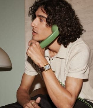 Un hombre con un teléfono verde lleva puesto un reloj Carraway de piel en color marrón.