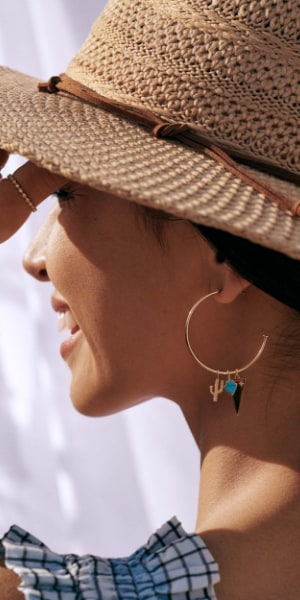 Eine Frau mit Hut trägt goldfarbene Creolen mit Charmanhängern.