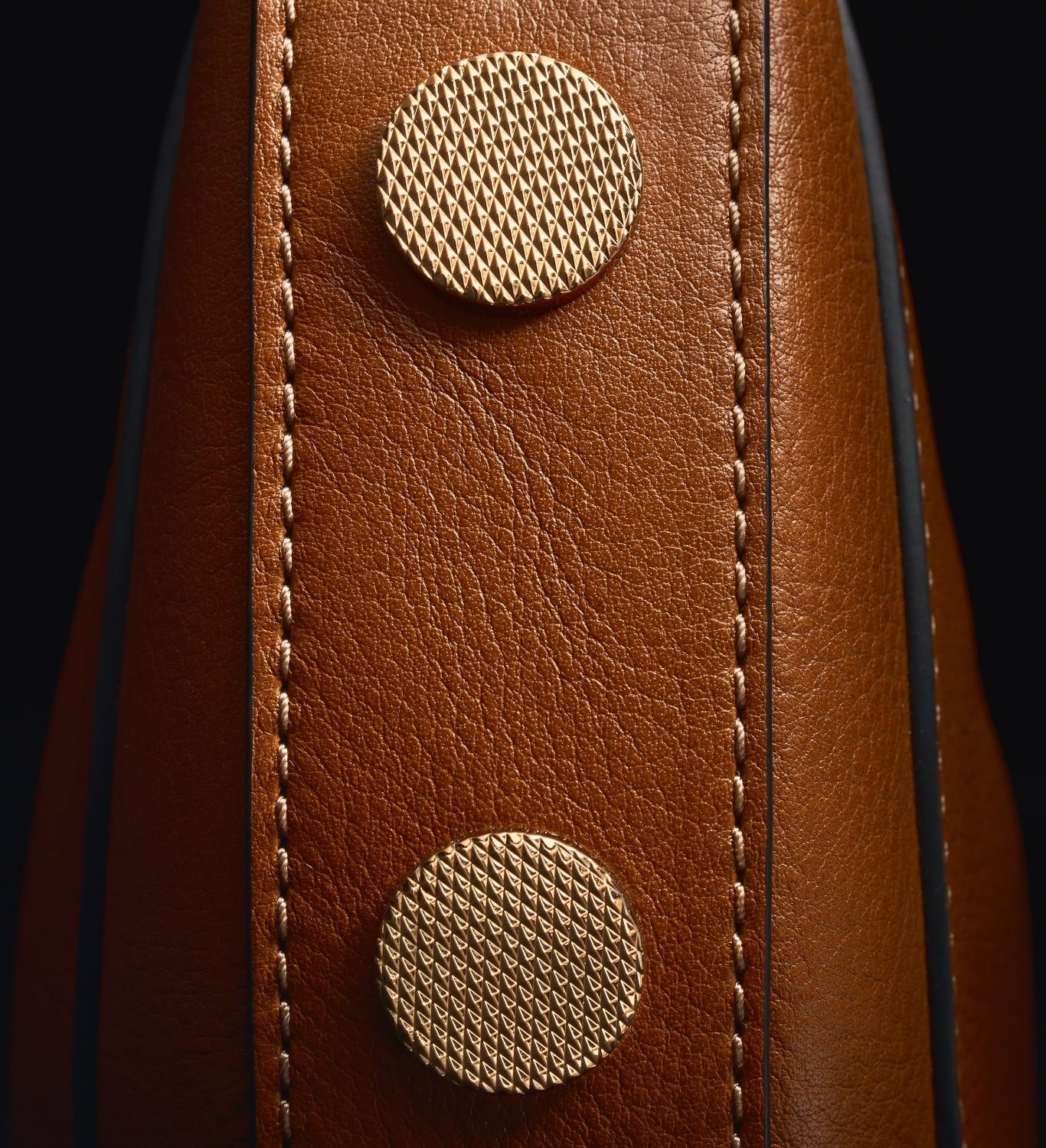 Two gold-tone knurled studs on a brown leather Harwell bag, overlaid with a sketch.