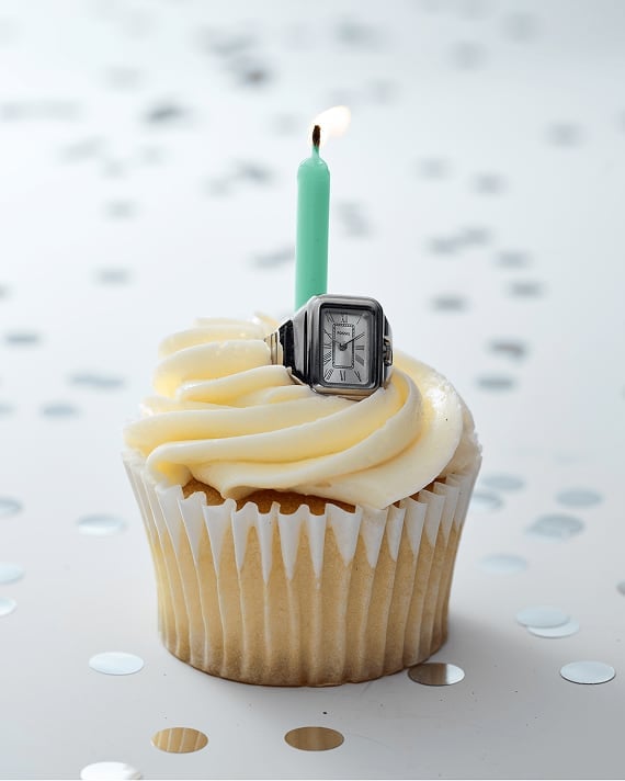 Silberfarbene Ringuhr Raquel auf einem wunderschön glasierten Cupcake mit einer brennenden Geburtstagskerze