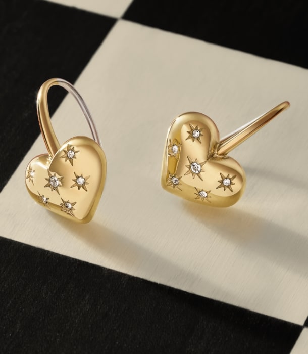 Gold-tone Sadie heart earrings resting on a black-and-white chess board.