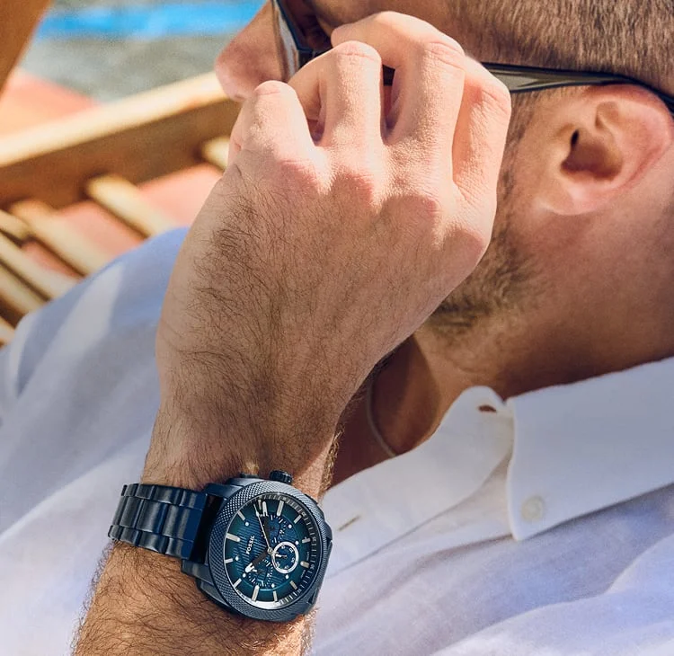 A dad relaxing on the water, adjusting his sunglasses and showcasing the Fossil Machine Chronograph watch in ocean blue.