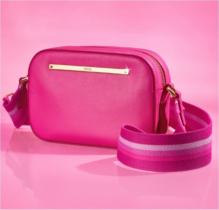 Un fond rose avec une fenêtre inspirée de la maison de Barbie™. À l’intérieur, on aperçoit notre sac pour appareil photo Liza en édition limitée Barbie™ x Fossil en cuir pleine fleur rose emblématique avec une large bandoulière sportive rayée rose, style années 90.