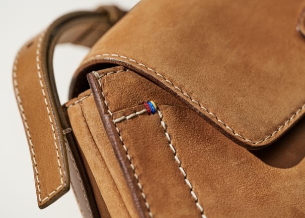 Una GIF con una borsa Tremont in pelle scamosciata marrone, con in primo piano l’imbastitura a tre colori e i bordi grezzi.