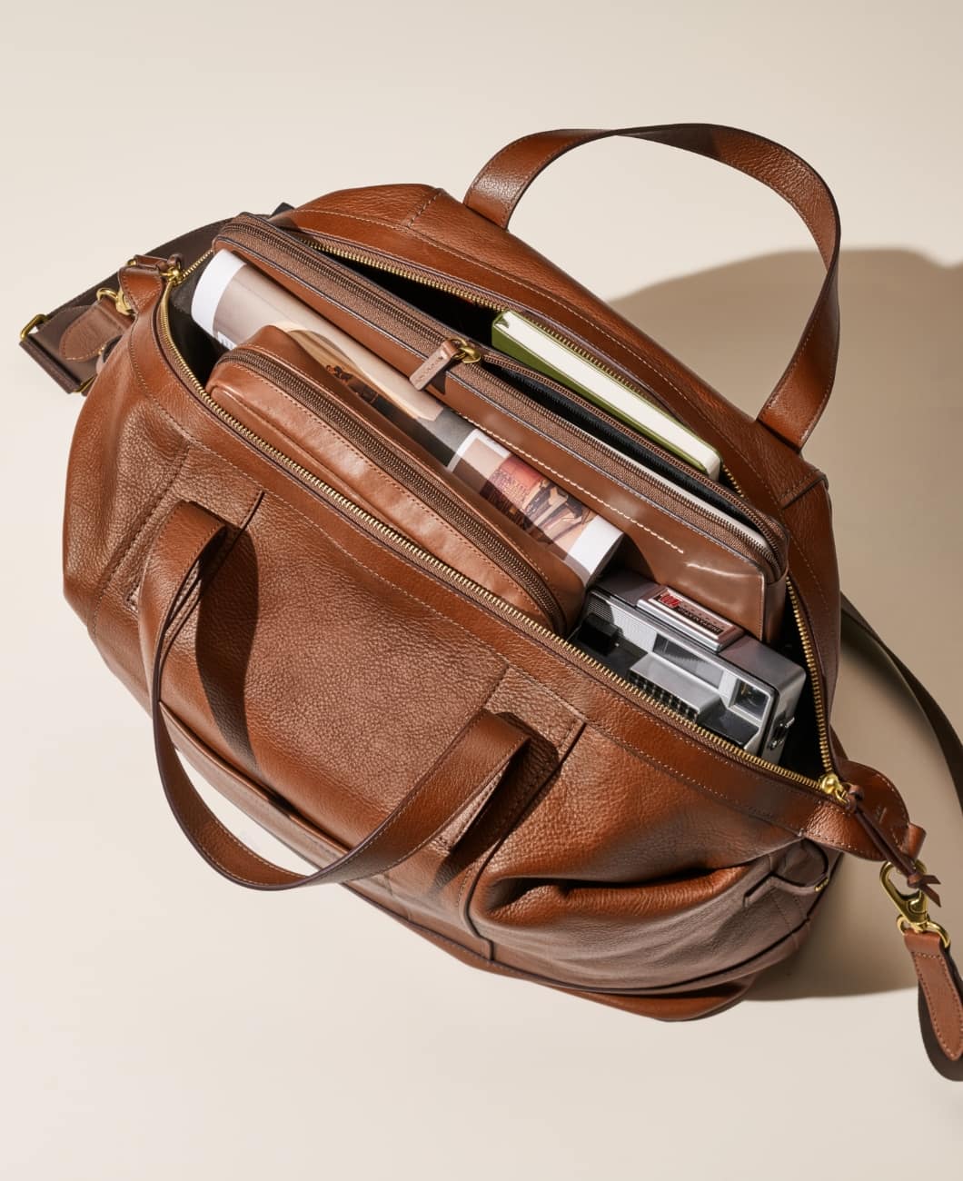 A man stands boldly with the Raeford duffle tossed over his shoulder. It has soft brown leather, a lightweight, convertible silhouette and a removable and adjustable crossbody or shoulder strap.