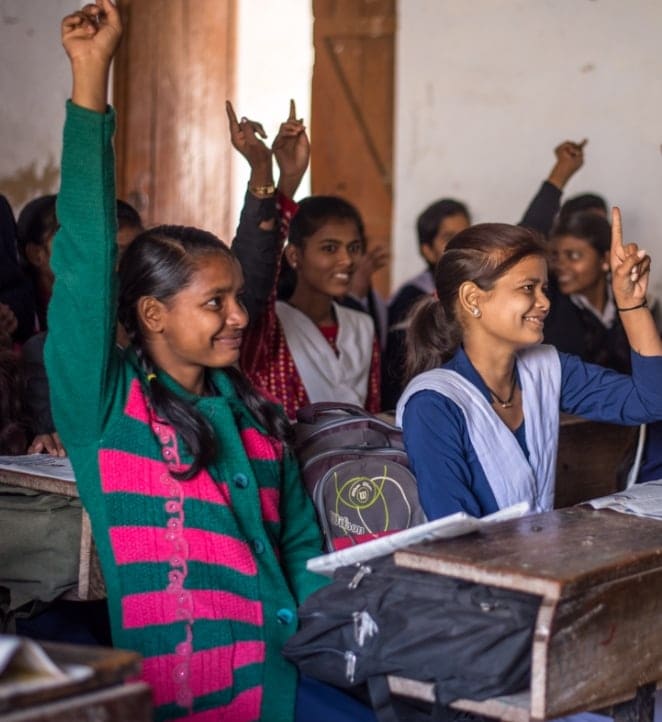 A group of young girls raising their hands in a classroom.