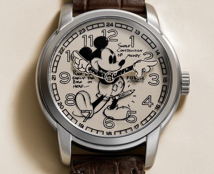 Une montre classique avec cadran blanc cassé caractérisée par Mickey Mouse de Disney illustré de façon à ressembler à un croquis au crayon. Les aiguilles dans la forme de ses mains tournent pour indiquer l’heure. La montre est placée sur un arrière-plan blanc cassé agencé.