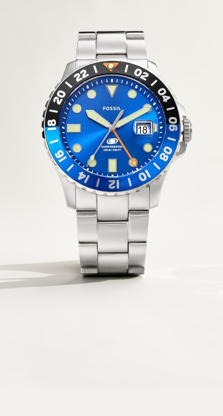 A closeup of the Fossil Blue GMT watch with a blue dial. A man wearing the silver-tone Fossil Blue GMT watch and a braided, beaded bracelet.