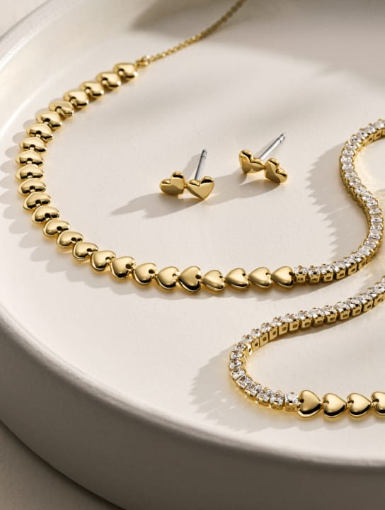 Gold-tone jewelry, including chains and heart-shaped stud earrings artfully arranged on a white jewelry tray.
