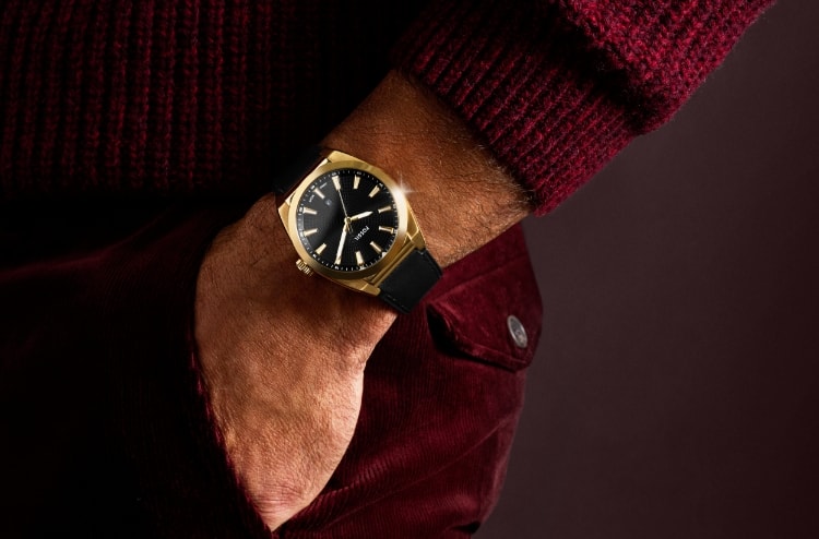 A man with his hand in his pocket wearing the gold-tone Everett watch with a black leather strap.