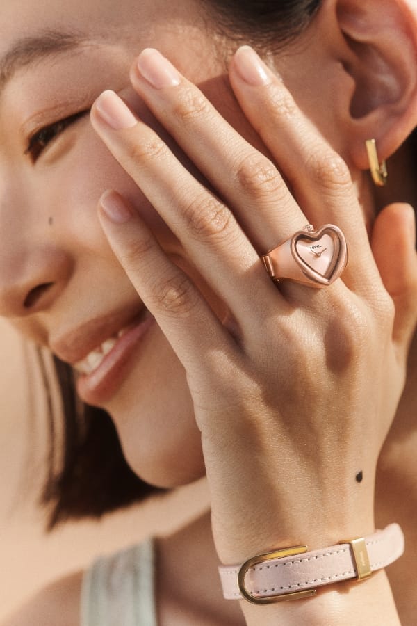 Une femme souriante portant une bague montre en forme de cœur ton or rose.