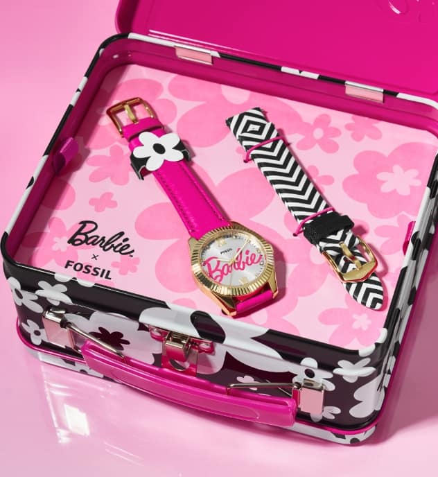 Image two. The tin is shown open to reveal a special-edition watch set inside. It features the scripted Barbie signature on the dial and leather strap in hot pink, displayed with interchangeable leather straps in a black-and-white chevron pattern.
