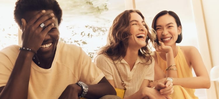 Un hombre y dos mujeres, sentados juntos y riendo, que llevan productos de Fossil. 