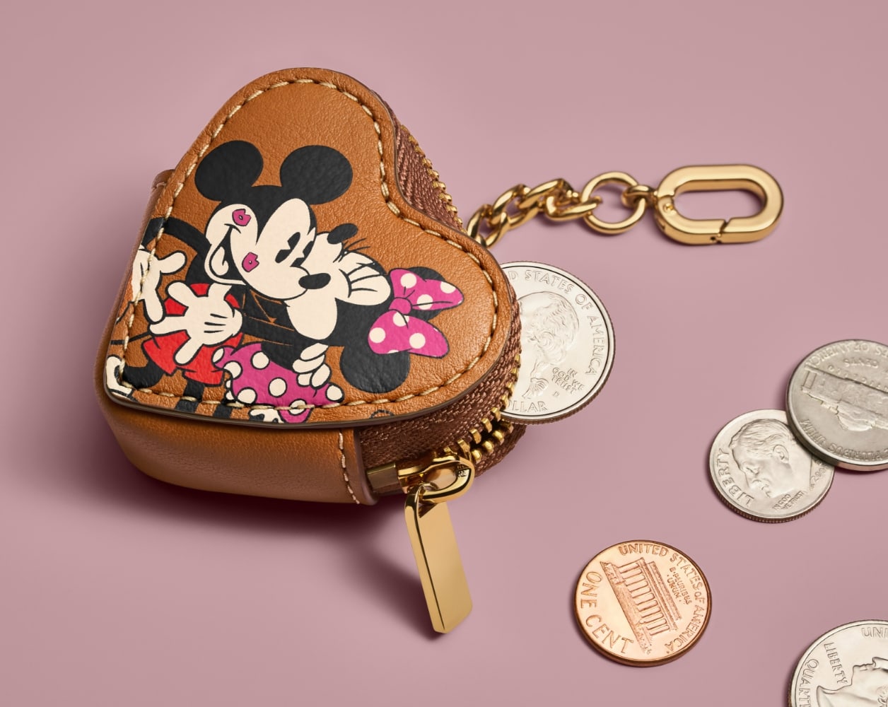 The brown leather heart-shaped coin purse, featuring an embossed graphic of Mickey Mouse and Minnie Mouse and showing various coins inside and around it.