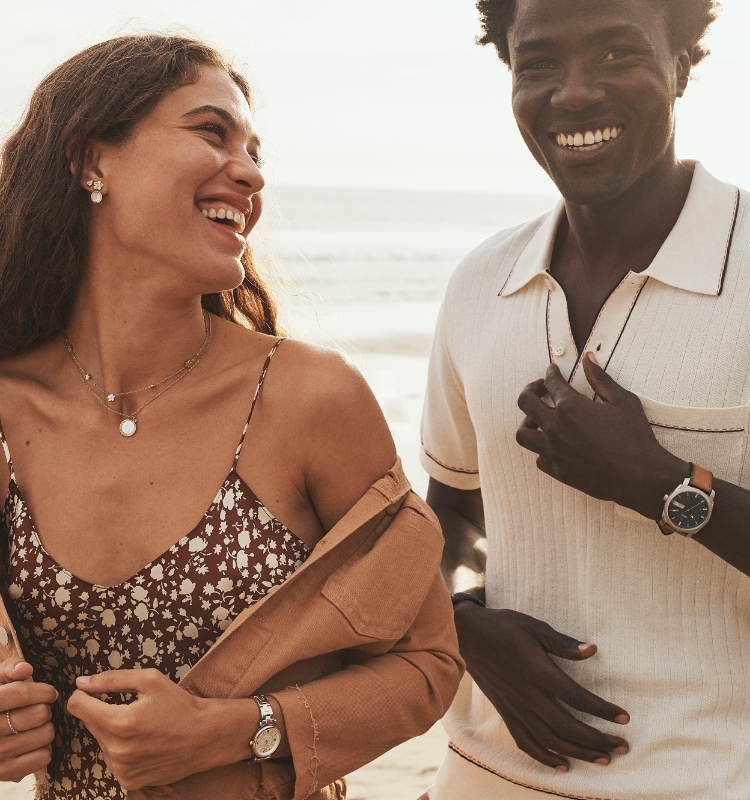 Un homme et une femme souriant sur la plage portant les nouveaux modèles d’été.