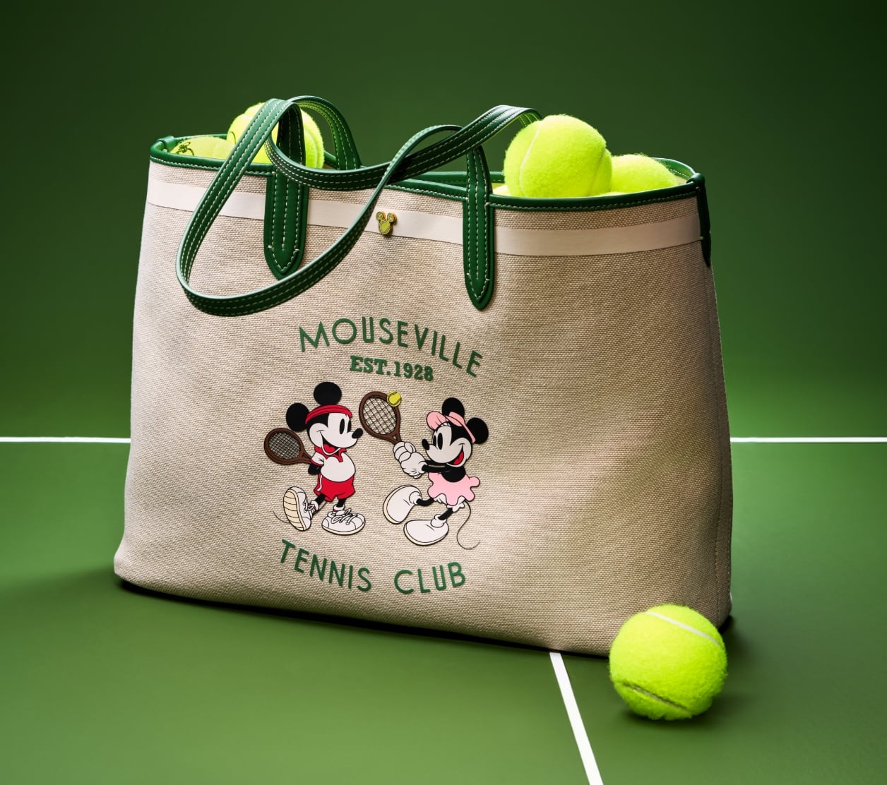 鮮やかなグリーンのテニスボールが詰め込まれ、テニスコートに置かれたスペシャルエディションのDISNEY TENNISトート。グリーンレザーのトリムが施されたコットンキャンバスのバッグには、テニスをするミッキーとミニーのグラフィックがスクリーンプリントであしらわれ、さらに「Mouseville Tennis Club, Est.1928」の文字が 入っています。