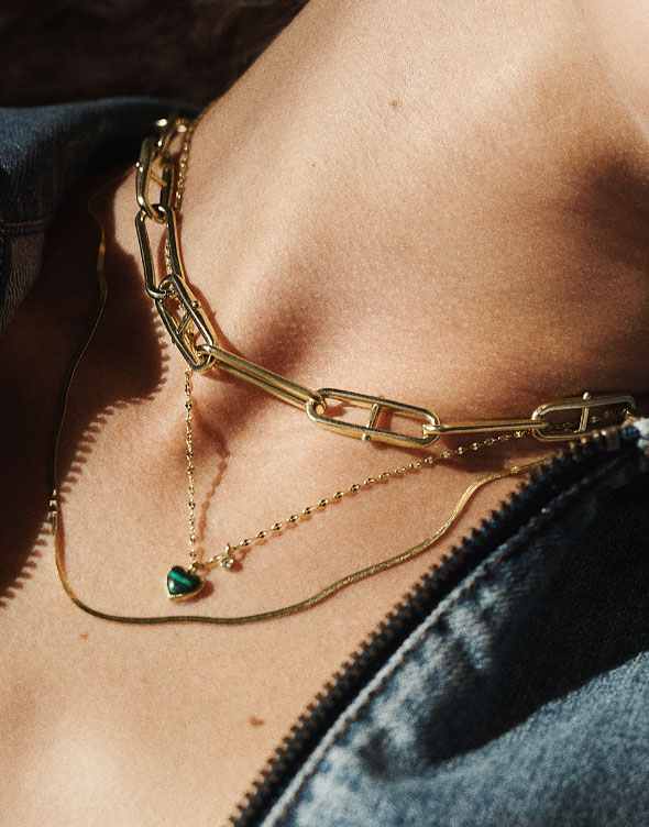 Primo piano del collo di una donna che indossa la collana a catena Heritage D-Link e la collana Modern Meadows con pendente a cuore in malachite verde ricostituita