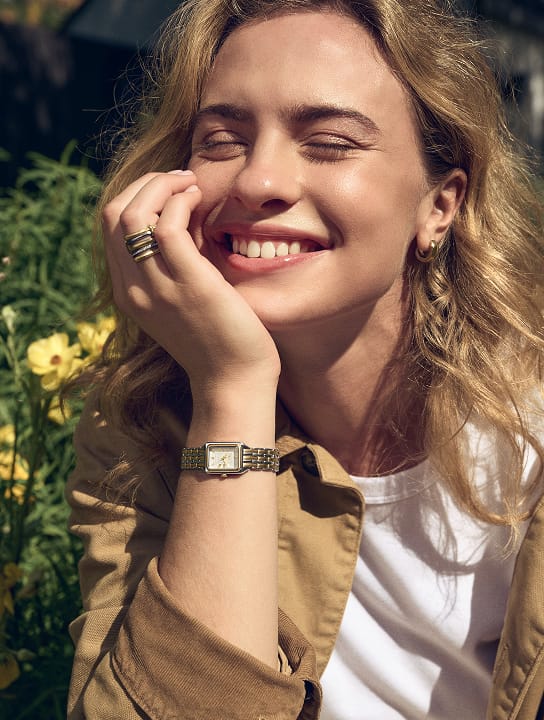 A woman smiling, resting her face on her hand, wearing the Fossil watch ring.