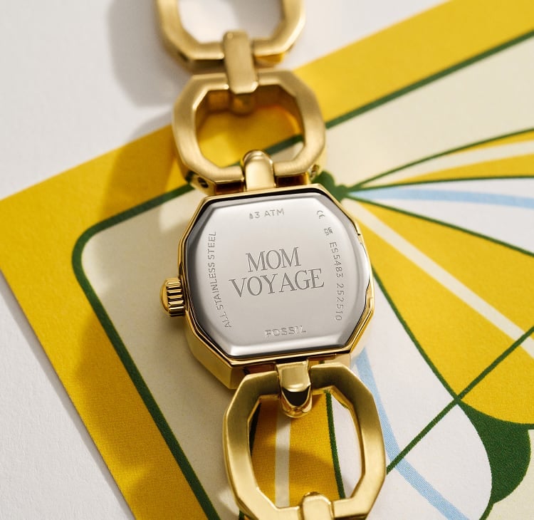 A Fossil watch caseback with the engraving 'Hello Sunshine.' Shown alongside a yellow and white postcard illustration of a beach chair, umbrella and lemonade sign.