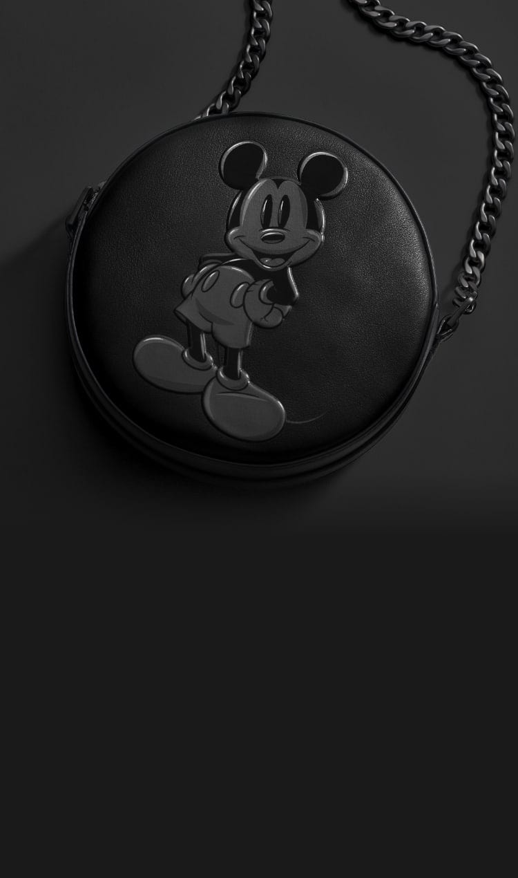 Eine komplett schwarze Canteen Bag aus Leder mit der Silhouette von Disneys Micky Maus. Die Tasche hat eine anthrazitfarbene Kette und wird vor einem schwarzen Hintergrund gezeigt.